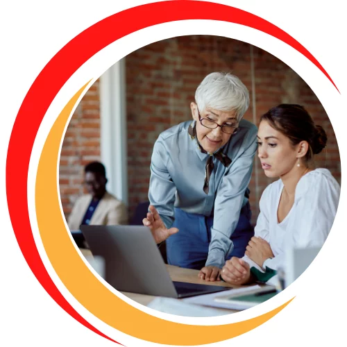 Senior professional discussing work with a younger employee on a computer.